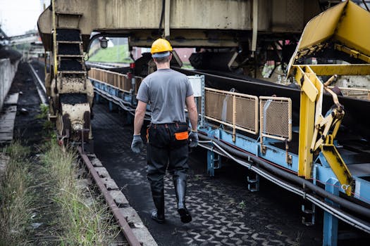 A worker in safety gear examines industrial machinery in an outdoor setting, showcasing industry work.