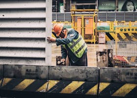 A construction worker in a reflective vest and hard hat at a busy urban construction site.